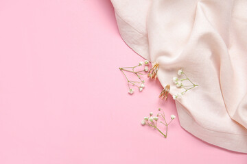 Beautiful golden earrings with gypsophila flowers and cloth on pink background