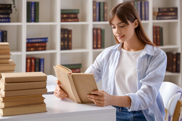 Happy female student reading books and studying at library