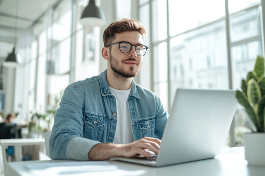 High-resolution brightly lit photorealistic candid photograph of a young marketer enjoying a productive workday on his laptop in a bright, modern office. The photograph is styled like a high-end