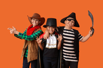 Cute happy boys in different costumes dressed for Halloween party showing gun gesture on orange background