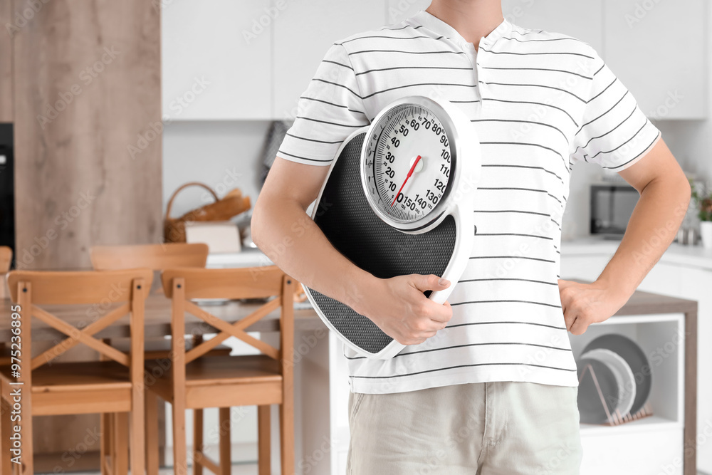 Wall mural young man with scales in kitchen. weight loss concept