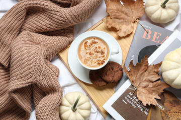 Cup of tasty pumpkin coffee with cookies, magazines and warm sweater on bed at home, top view