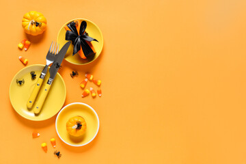 Festive table setting for Halloween celebration with gift box, candies and pumpkins on orange background