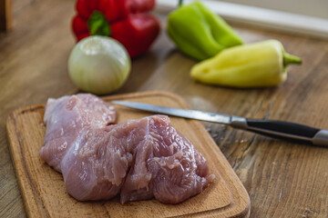 A piece of chicken fillet on a cutting board, a knife and vegetables on the side