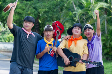 Young asian teenboys hold acoustic guitar, ukulele and notebook, standing together in their school park to get relaxing after doing the volunteers  at school.