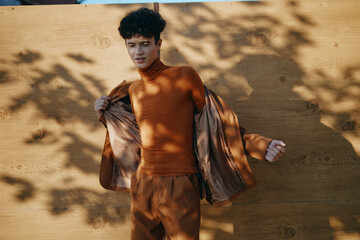 Stylish young man in brown outfit standing against wooden background with playful shadows