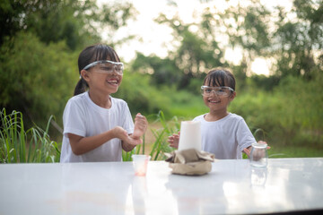 Two young girls excitedly play with a small volcano experiment, laughing as foam erupts.
