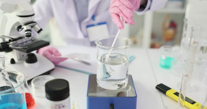 Scientist analyzes water sample using PH test strips in laboratory. Chemist compares color pattern on paper with table at workplace