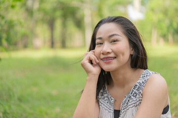 Happy young woman sitting looking at camera looking cheerful and relaxed in a quiet environment in the middle of a garden. Summer time. Spending time in nature. Maintaining a healthy lifestyle