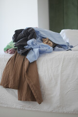 A disorganized and messy pile of various clothes scattered on a bed in the bedroom