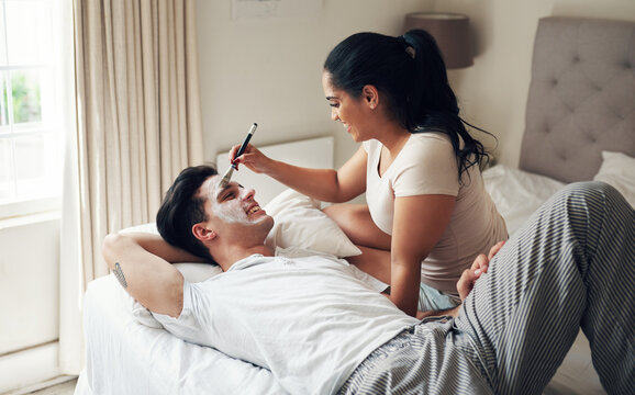 Couple, man and face mask treatment in home for hydration, dermatology or skincare on bed. Happy people, facial serum and product application in bedroom for bonding, grooming or fun activity in house