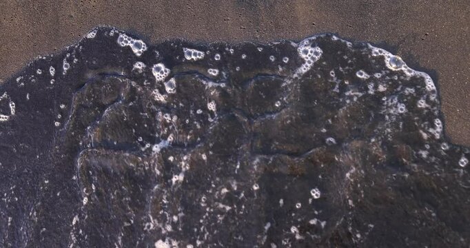 Ocean waves erase short inscription 2024 from wet sand. Powerful symbol of inevitable passage of time and arrival of new beginnings