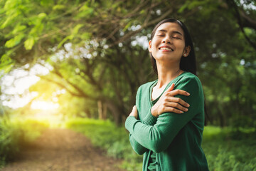 confident asian woman embraces self-love, standing peacefully in serene park at sunset. joyful...