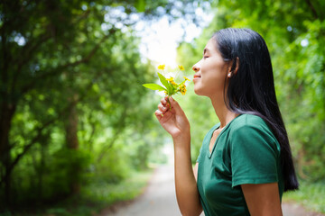 A cheerful young asian woman enjoys a sunny day outdoors, holding a vibrant bunch of yellow flowers. Smiling in a green field, she embodies the joy and freedom of summer in the countryside.