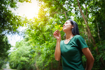 Fototapeta premium A cheerful young asian woman enjoys a sunny day outdoors, holding a vibrant bunch of yellow flowers. Smiling in a green field, she embodies the joy and freedom of summer in the countryside.