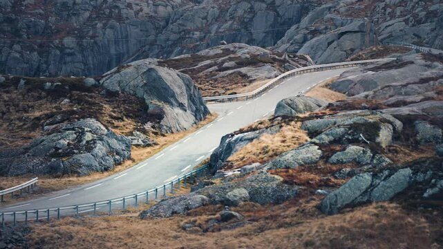 A narrow asphalt road goes through the barren rocky landscape. Withered grass between the dark chipped rocks.
