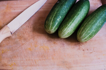 Pile of Fresh cucumbers with kitchen knife on a wooden cutting board, natural presentation, possibly in preparation for slicing or cooking.