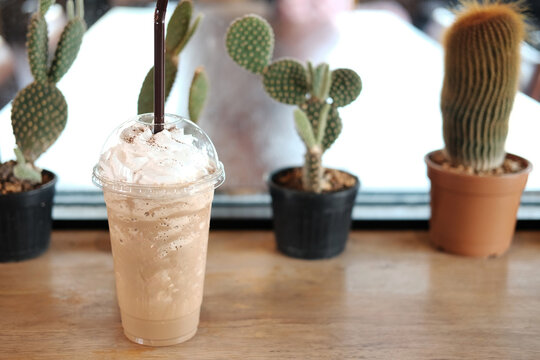 Fresh ice latte frappe coffee with bulb in plastic glass on wooden table and cactus plant decorate on counter in cafe. Copy space