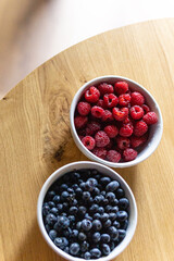 raspberries and blueberries in white bowls on the table