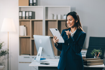 Young smart businesswoman holding digital tablet while holding coffee cup and standing in the modern office room.