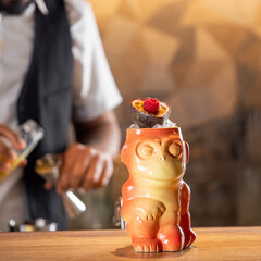 Tiki Drink Cocktail. One tropical tiki cocktail on bar counter. Tiki cocktail in monkey mug decorated fig and raspberry on bar in night club