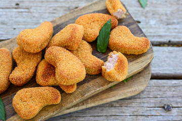
 Crispy oven baked  chicken nuggets and ketchup. Breaded chicken fillets  with chilly peppers and fresh basi on wooden rustic background