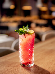 Red non-alcohol cocktail with crushed ice in glass on wooden bar counter in restaurant interior. Gin alcohol cocktail decorated lime and mint. Pink cold alcoholic cocktail in bar or nightclub