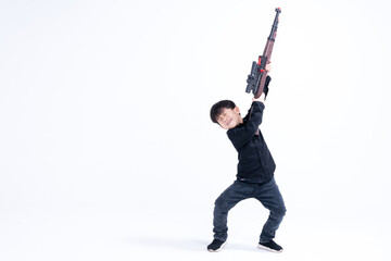 Young boy in playful pose holding a toy rifle against a white studio background.