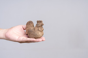 Hand holding a carved wooden rooster figurine against a plain background.