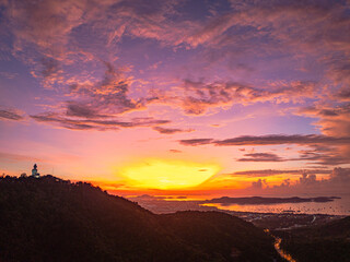 Arial view stunning sunrise above Phuket big Buddha on the mountain. A breathtaking panoramic view of a vibrant sunrise casting warm hues over a coastal town, with the sea reflecting of the sky