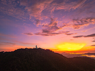 Arial view stunning sunrise above Phuket big Buddha on the mountain. A breathtaking panoramic view of a vibrant sunrise casting warm hues over a coastal town, with the sea reflecting of the sky