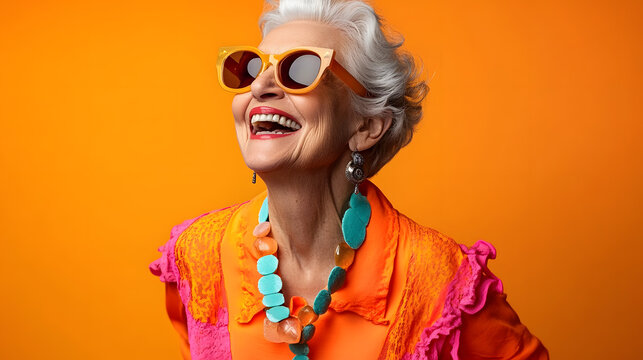 Happy senior woman in colorful orange outfit, cool sunglasses, laughing and having fun in fashion studio