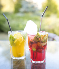 Two glasses of mixed drinks sit on a table, one of which is a pink drink