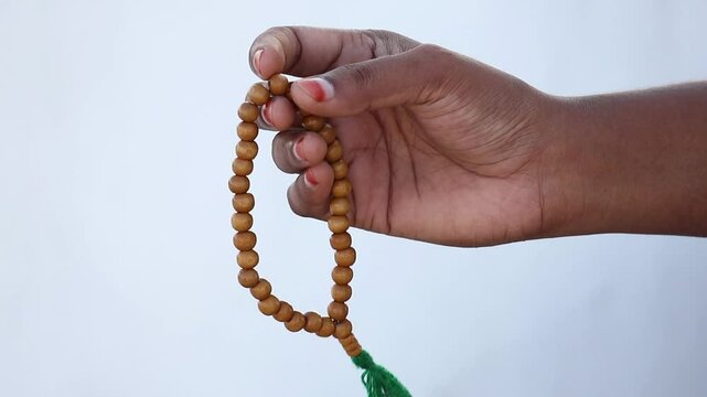 Muslim woman's hand holding wooden prayer beads (or tasbih) and counting them with her finger. Islamic concept for dhikr or zikr recitation.