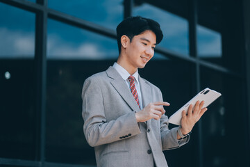 Fototapeta premium Serious businessman looking at paper documents in front of office building. Focused male manager checking reports before work while standing outdoors.