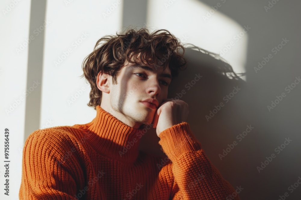 Wall mural Contemplative young man in orange sweater sitting in soft sunlight