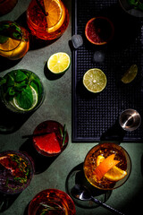 Alcoholic cocktails and bar tools on green background, top view