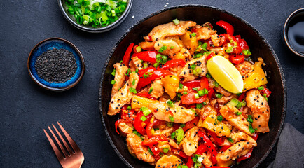 Stir fryed chicken slices with pineapple, paprika, chives, garlic, ginger, soy sauce and sesame seeds. Black background, top view