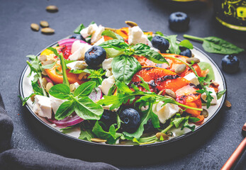 Foodie food salad with grilled peaches, blueberries, red onion, feta cheese, basil and arugula on black background, top view