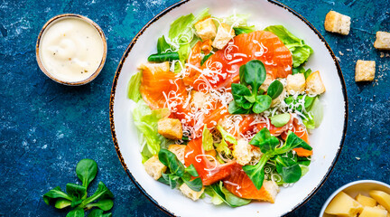 Foodie food caesar salad with salmon, iceberg  lettuce, croutons, grated parmesan with dressing. Blue background, top view