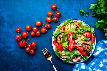 Vegan salad with grilled vegetables, tomatoes and mixed herbs. Blue background, top view