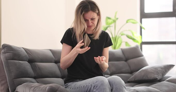 Woman checks empty wallet and cries sitting alone on sofa. Blonde lady loses money savings during financial crisis. Broken female at home