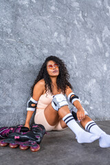 Sportive woman sitting leaning on urban wall with inline skates