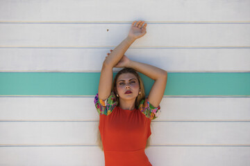beautiful young woman with long hair in an orange dress, on the white and turquoise striped wooden...