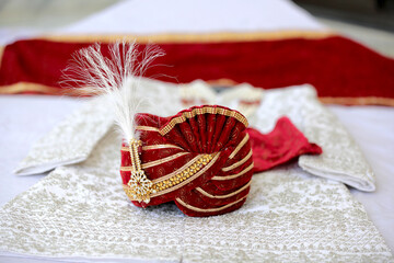 An elegant red groom's turban adorned with intricate embroidery and pearls, symbolizing the regal attire of an Indian wedding. The scene exudes sophistication and cultural charm.