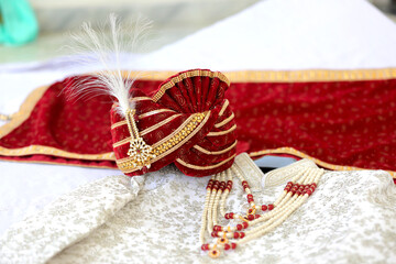 An elegant red groom's turban adorned with intricate embroidery and pearls, paired with traditional embroidered sherwani, symbolizing the regal attire of an Indian wedding. 