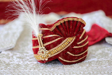 An elegant red groom's turban adorned with intricate embroidery and pearls, symbolizing the regal attire of an Indian wedding. The scene exudes sophistication and cultural charm.