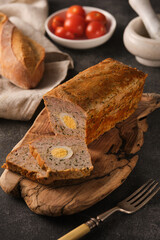 A rustic table showcasing a homemade meatloaf with boiled eggs, fresh bread, and cherry tomatoes under soft, natural light