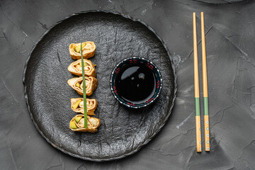 Tamagoyaki or a traditional Japanese omelet roll with avacado and cheese on a black mica plate with soy sauce and chopsticks.