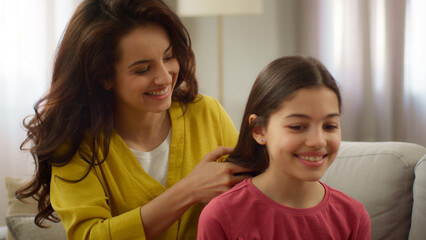 Caring loving Caucasian mother female woman sister braiding hair making hairstyle coiffure smiling...
